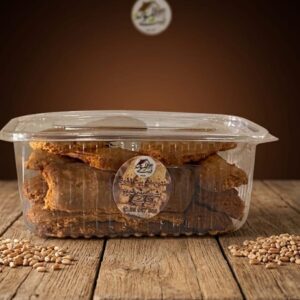 Un biscuit tunisien traditionnel appelé bchkito dans sa boîte transparente posée sur une table en bois.