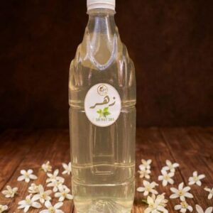 Une bouteille Une bouteille d'eau de fleur d'oranger artisanale entourée de boutons de fleurs blanches sur une table en bois.