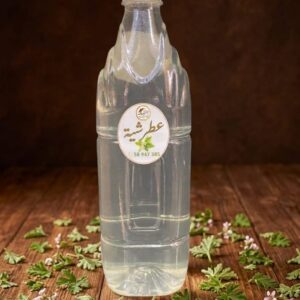 Bouteille d'eau de géranium rosat artisanale (Atechia) posée sur une table en bois et entourée de feuilles et de fleurs fraîches.